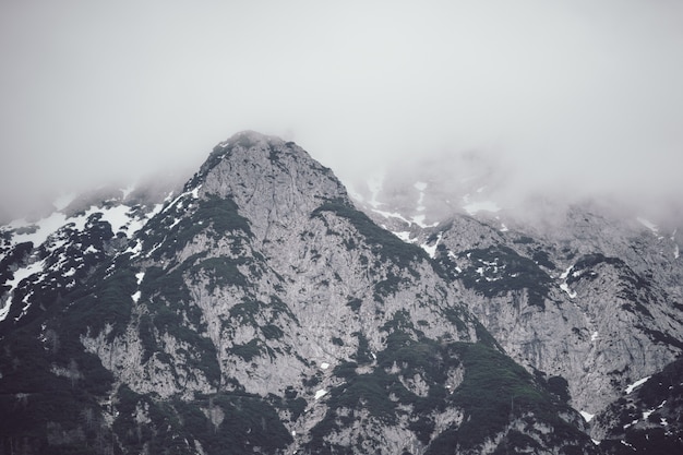 Низкий угол обзора высокой скалистой горы, покрытой густым туманом