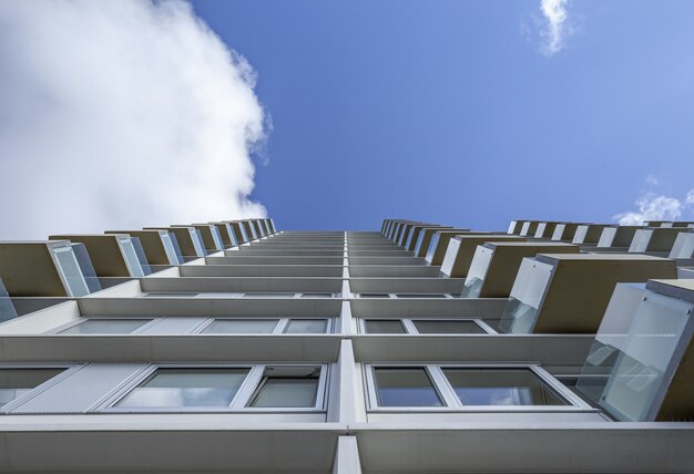 Low angle shot of a tall white building with glass balconies under the clear blue sky