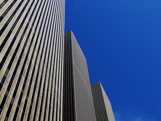 Free photo low angle shot of three identical skyscrapers under the bright blue sky