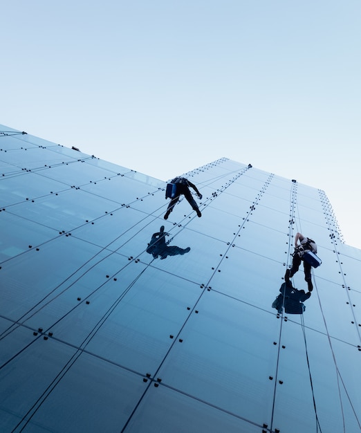 Low angle shot of two persons rappelling at the side of a tall building