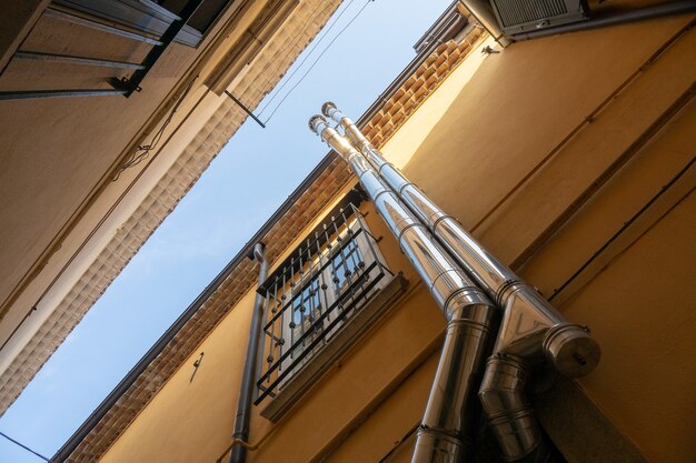Снимок под низким углом двух труб, поднимающихся по зданию рядом с окном