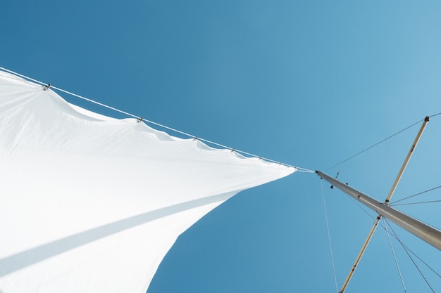 昼間の晴れた空の下でボートのマストに白い帆のローアングルショット