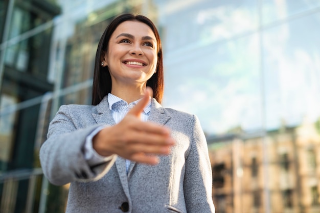Low angle of smiley businesswoman giving hand for handshake outdoors