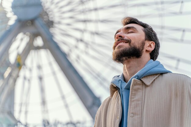 Low angle of smiley man outdoors next to ferry wheel