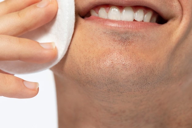 Low angle smiley man using cotton pad