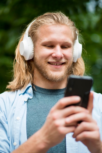 Low angle of smiley man with smartphone and headphones