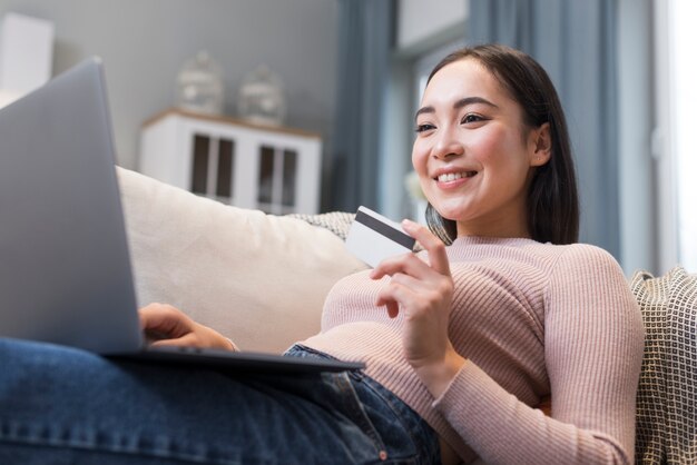 Low angle of smiley woman holding credit card and laptop