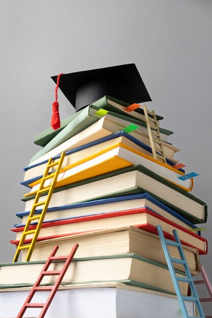 Низкий угол сложенных книг, выпускной колпак и лестницы для дня обучения
