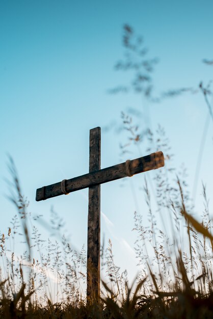 Low angle vertical shot of a hand made wooden cross in a grassy field with a blue sky in background