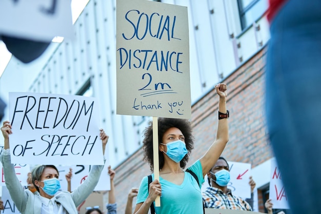 Vista ad angolo basso della donna afroamericana con il pugno alzato che partecipa a manifestazioni durante l'epidemia di coronavirus