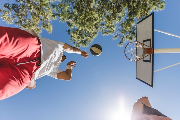 Низкий угол зрения баскетболист, бросающий мяч против голубого неба