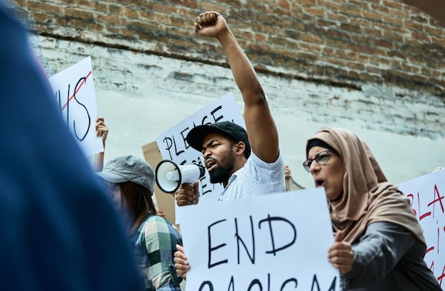 Low angle view of black protester with raised fist shouting through megaphone on antiracism demonstrations