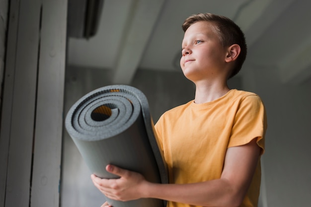 Low angle view of boy holding rolling grey exercise mat