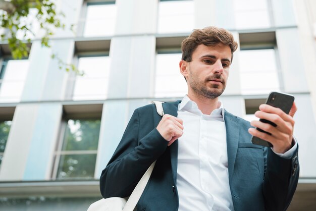 Low angle view of a businessman standing in front of building looking at mobile phone