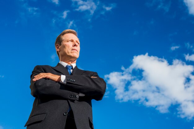 Low angle view of businessman standing with folded arms against sky