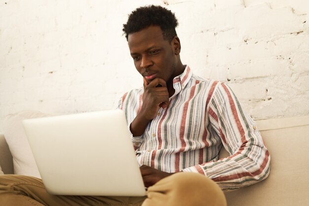 노트북과 함께 소파에 앉아 집중 매력적인 젊은 아프리카 계 미국인 학생의 낮은 각도보기