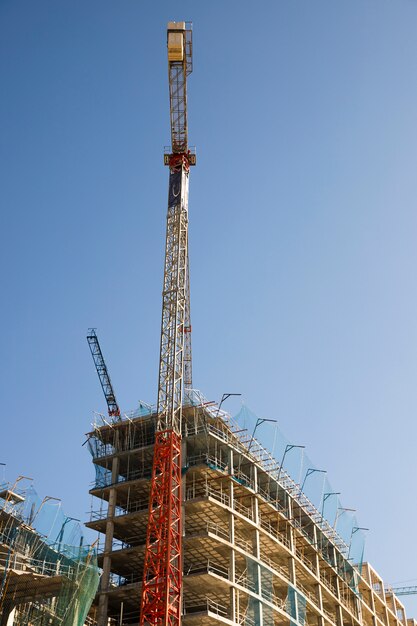 Low angle view of construction crane near the site against blue sky