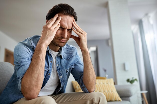 Low angle view of distraught man holding his head in pain while sitting in the living room