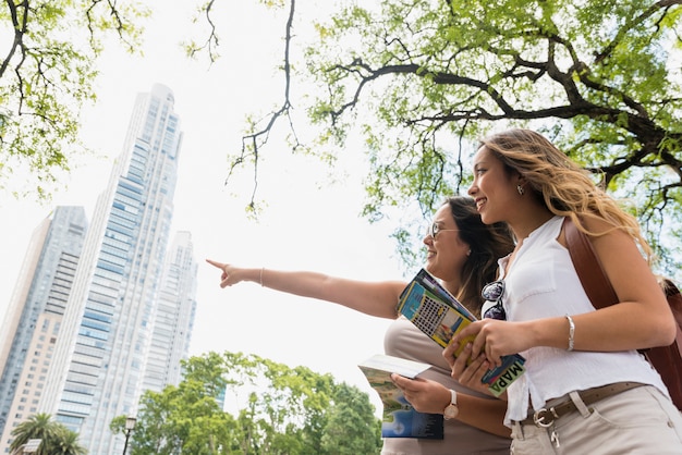 Free photo low angle view of female holding map in hands looking at her female pointing at something