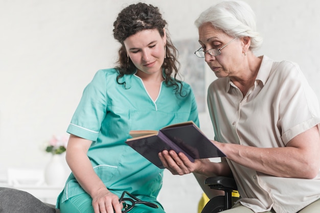 Low angle view of female nurse looking at senior woman reading book