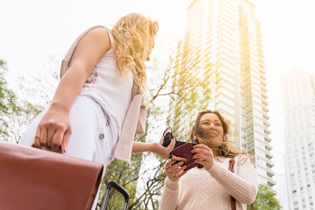 Low angle view of female tourist giving passport to her friend against high rise building