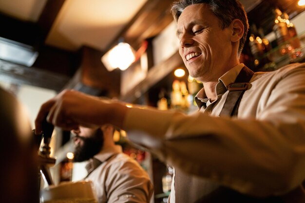 Low angle view of happy barista pouring draft beer while working in a pub.