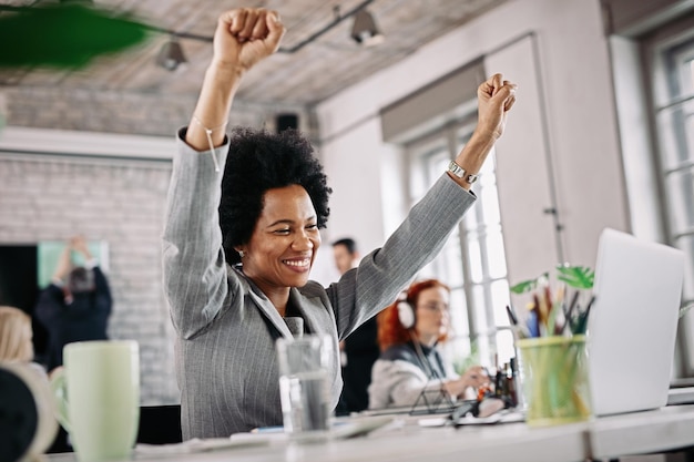 Foto gratuita inquadratura dal basso di felice imprenditrice nera che lavora in ufficio e celebra il suo successo con le braccia alzate