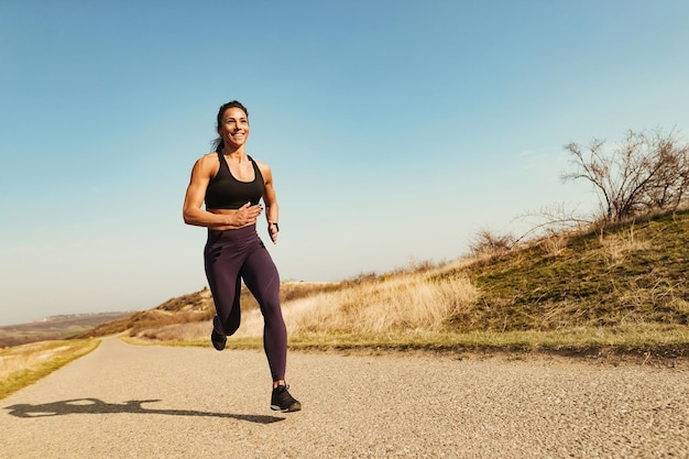 Low angle view of happy muscular build sportswoman running on the road Copy space