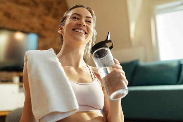 Низкий угол обзора счастливой спортсменки, пьющей воду во время тренировки дома