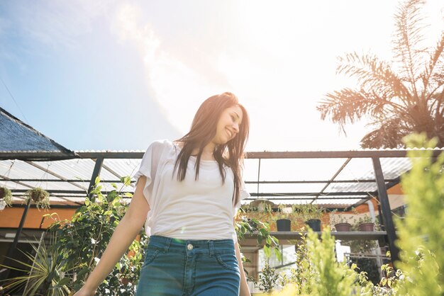 Low angle view of a happy woman surrounded with plants standing in greenhouse