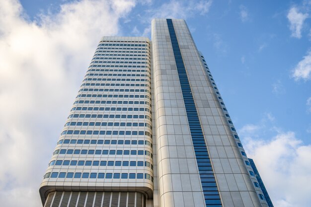 Low angle view of a high rise building with blue windows under a cloudy sky and sunlight