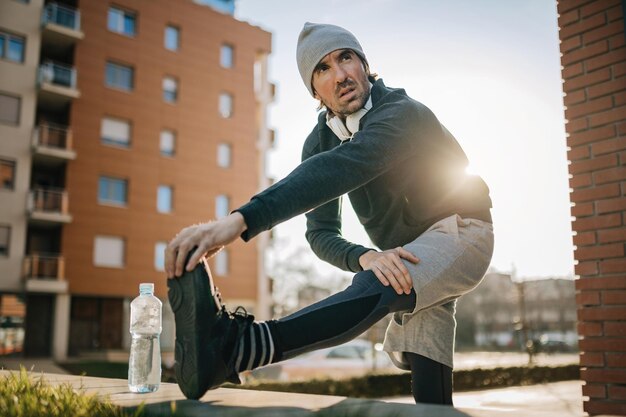 Low angle view of male athlete warming up and stretching his leg while preparing for sports training outdoors