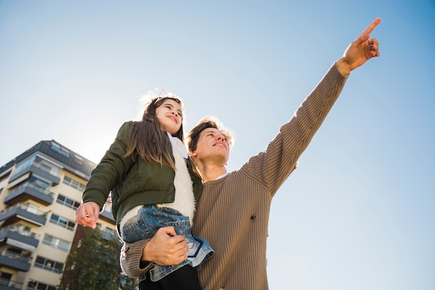 Low angle view of a man pointing while carrying his daughter