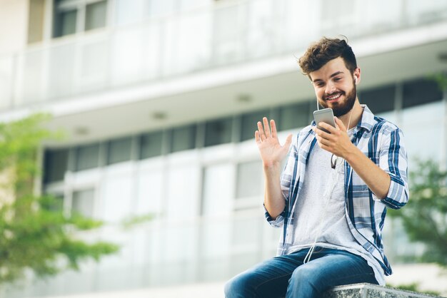 大学のキャンパスに座っている友人にビデオ通話男の低角度のビュー