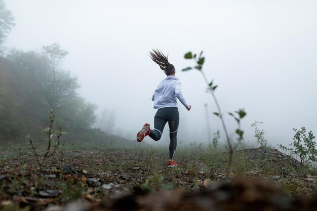 안개 낀 날씨 복사 공간 동안 자연에서 달리는 동기부여된 스포츠우먼의 낮은 각도 보기