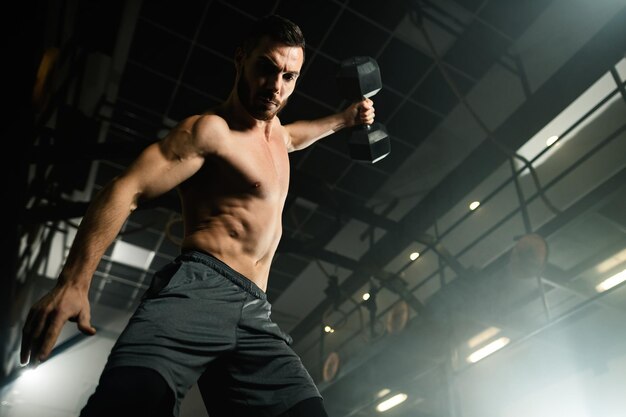 Low angle view of muscular build man exercising strength while working out with dumbbell in health club