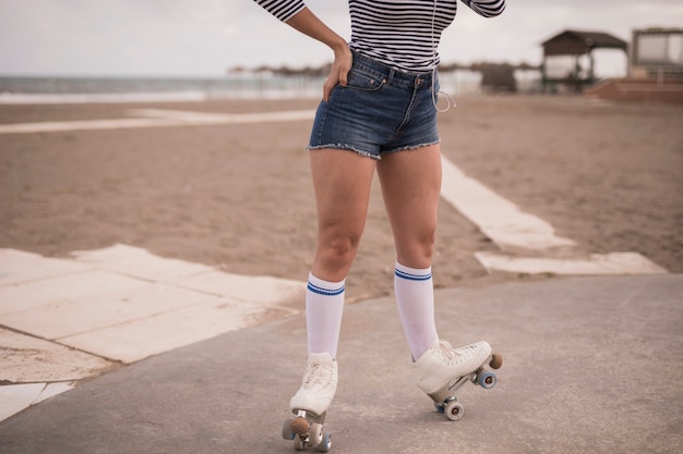 Бесплатное фото Низкий угол зрения женщины, балансируя на роликовых коньках на пляже
