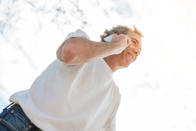 Low angle view of smiling man talking on mobile phone standing under the sky