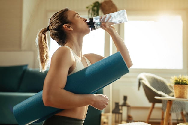 Low angle view of thirsty sportswoman drinking water after exercising at home.