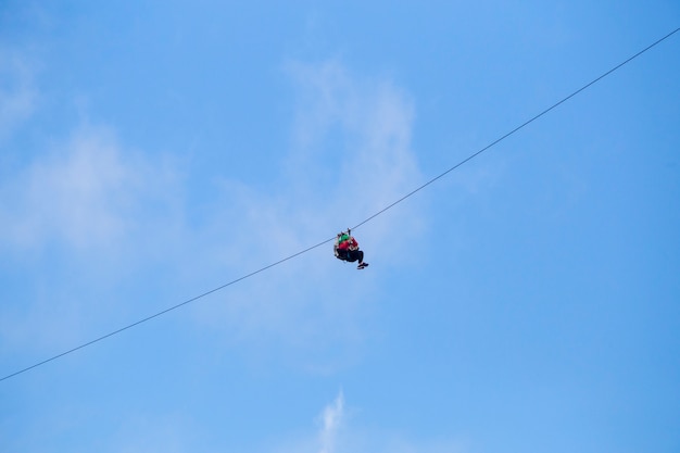 Low angle view of tourist riding a zip line adventure against blue sky