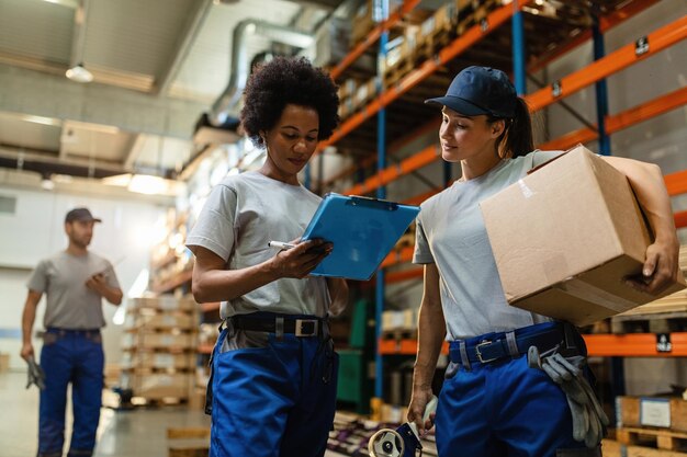 Low angle view of two female workers reading delivery schedule list while working in distribution warehouse