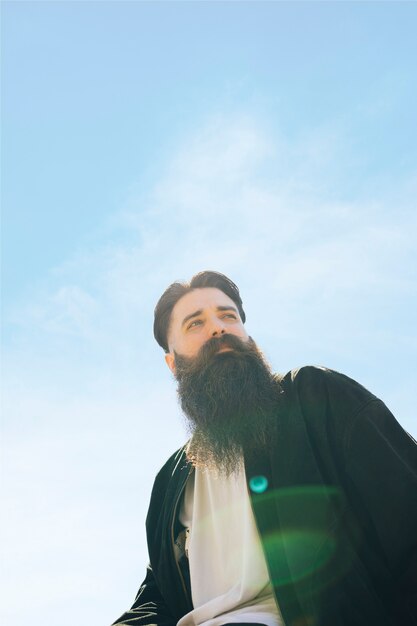 Free photo low angle view of a young bearded man standing under blue sky