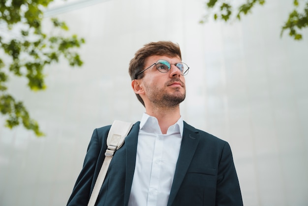 Low angle view of a young businessman standing against wall looking away