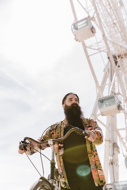 Free photo low angle view of a young man riding cycle near ferris wheel