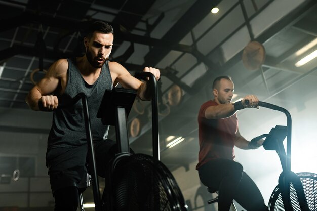 Low angle view of young sportsmen cycling on exercise bikes while working out in a gym