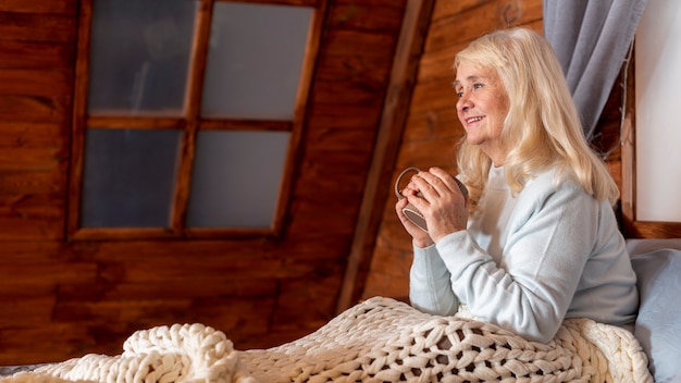 Free photo low angle woman in bed drinking tea