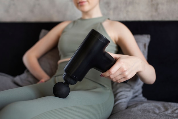 Low angle woman using massage gun on leg