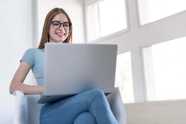 Foto gratuita donna di angolo basso con i vetri che esaminano il suo computer portatile