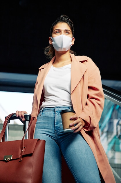 Free photo low angle of woman with medical mask and luggage at the airport