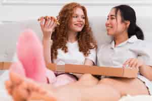 Free photo low angle women in bed eating pizza